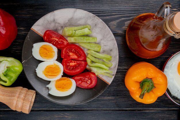 Top view of boiled halved eggs on a plate with peppers with apple vinegar on a wooden background