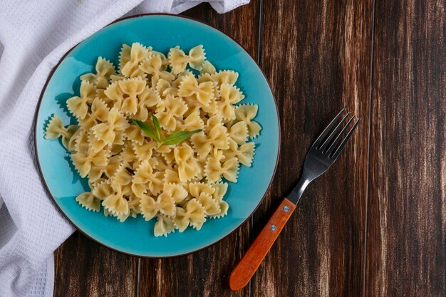 Top view of boiled pasta on a blue plate with a fork on a wooden surface