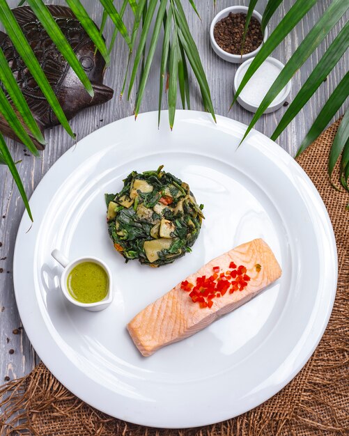 Вид сверху отварной красной рыбы с тушеной зеленью и соусом на тарелке