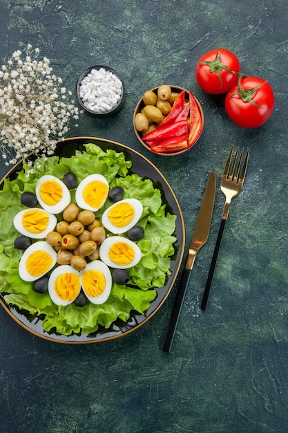 top view boiled sliced eggs with green salad and olives on dark blue background