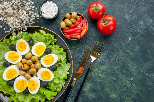 top view boiled sliced eggs with green salad and olives on dark blue background