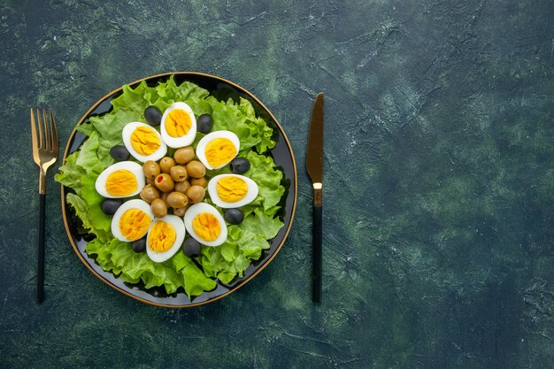 вид сверху вареные нарезанные яйца с оливками и зеленым салатом на темно-синем фоне