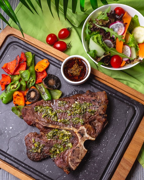 Top view bone steak with grilled vegetables and sauce on the board with vegetable salad