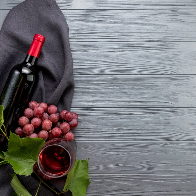 Вид сверху бутылка вина с бокалом и гроздью винограда