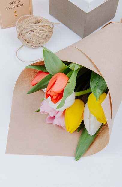 Top view of a bouquet of colorful tulip flowers in a craft paper with gift boxes and rope on white background