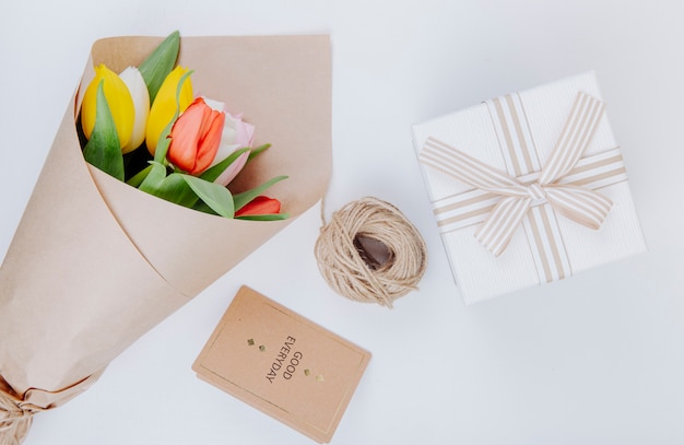 Free photo top view of a bouquet of colorful tulip flowers in a craft paper with a postcard gift box and rope on white background