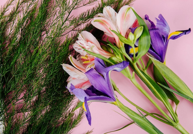 분홍색 배경에 아스파라거스와 어두운 보라색 아이리스와 alstroemeria 꽃의 꽃다발의 상위 뷰