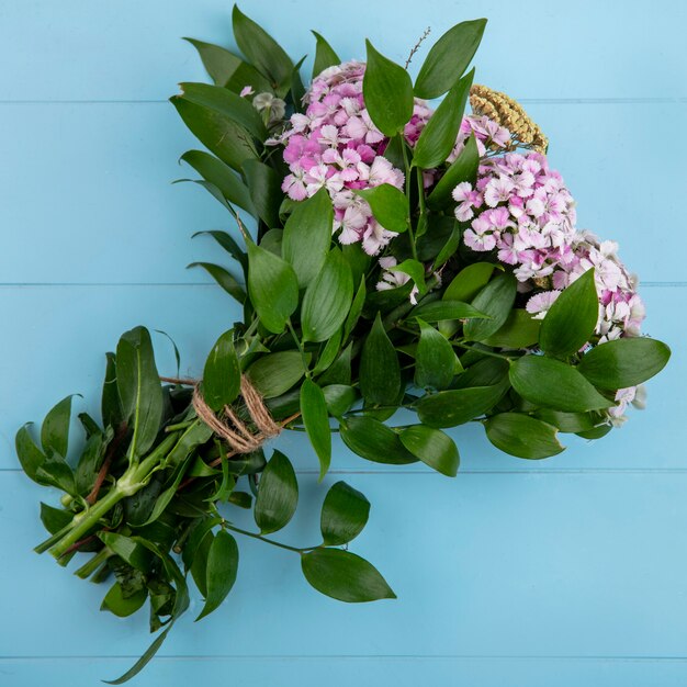 Top view of bouquet of light purple flowers with leaf branches on a light blue surface