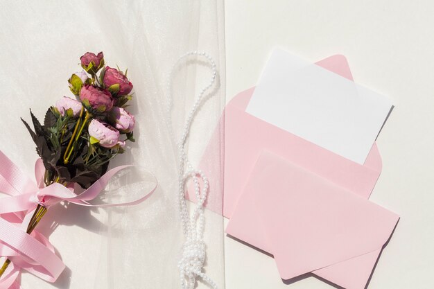 Top view bouquet of roses on veil next to wedding invitations