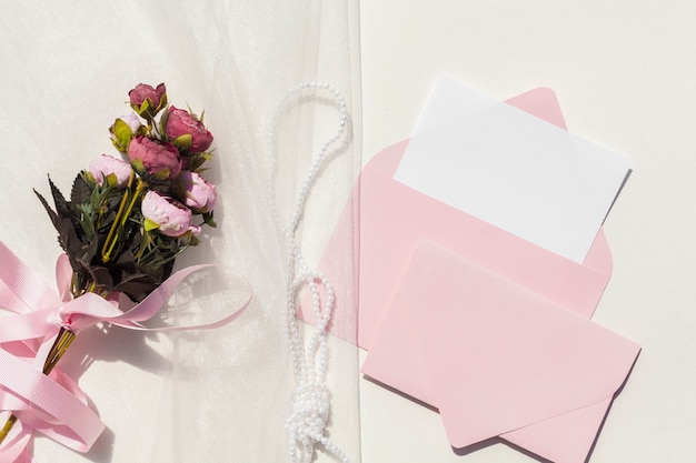結婚式の招待状の横にあるベールにバラの上から見る花束