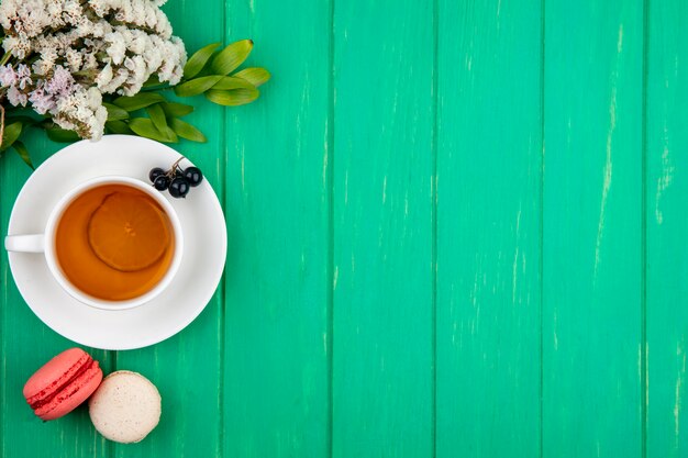 Top view of bouquet of white flowers with a cup of tea with macarons on a green surface