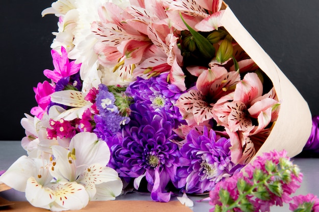 Top view of a bouquet of white and pink color alstroemeria and chrysanthemum flowers in craft paper on dark background