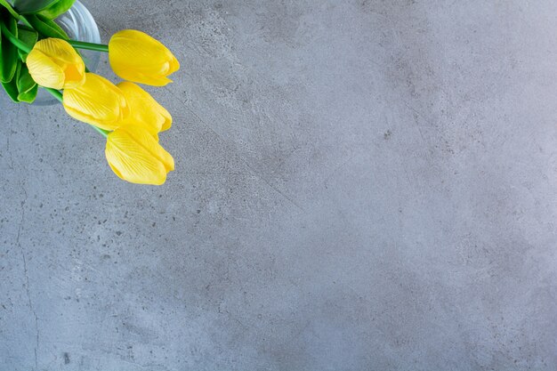 Top view of a bouquet of yellow tulips in a glass vase on the gray background.