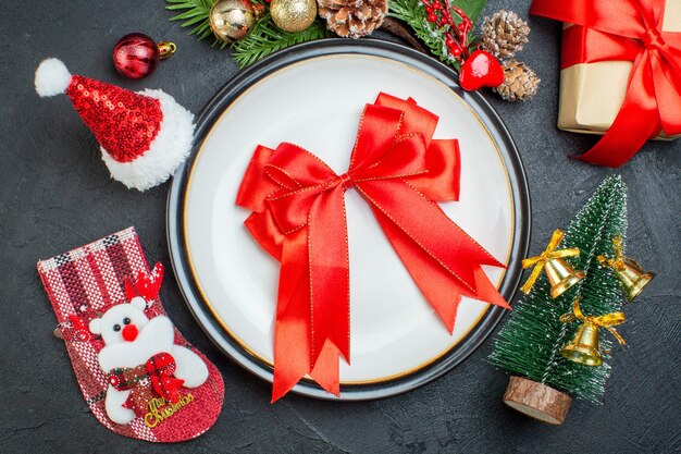 활의 상위 뷰는 저녁 식사 접시에 빨간 리본 모양의 크리스마스 트리 전나무 가지 침 엽 수 콘 선물 상자 산타 클로스 모자 크리스마스 양말 검은 배경에