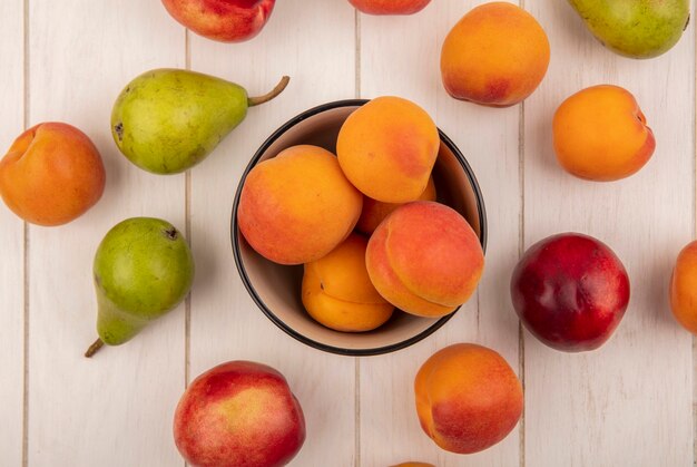 Top view of bowl of apricots and pattern of fruits as peach apricot and pear on wooden background