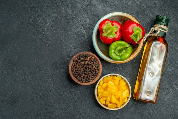 Free photo top view of bowl of bell peppers on the right side with herb and vegetable bowls oil bottle on side on green table