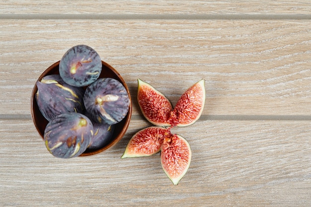 Top view of the bowl of black figs and slices of figs on a wooden table