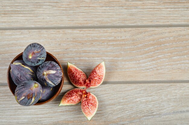 Top view of the bowl of black figs and slices of figs on a wooden table