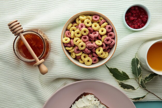 Top view of bowl of cereal with oats orange juice red currant jam around on white background