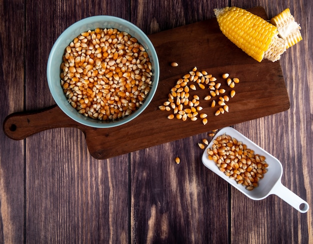 Free photo top view of bowl of corn seeds cut corn on cutting board with spoon full of corn seeds on wood