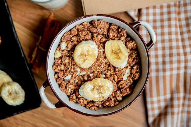 Top view of bowl full of nuts and sliced bananas on wooden surface