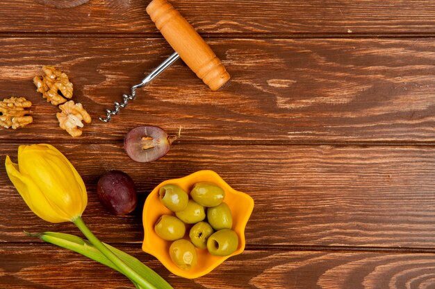 Top view of bowl of olive with walnut grape corkscrew and flower on wooden background with copy space