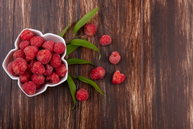 Top view of bowl of raspberry with leaves on wood with copy space