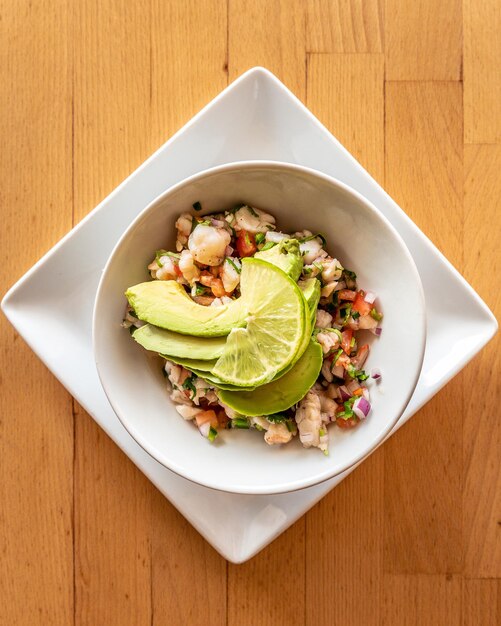 Top view of a bowl of seafood with lime and avocado