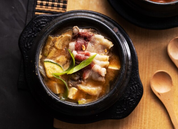 Top view of a bowl of soup with pork and zucchini on the tabl