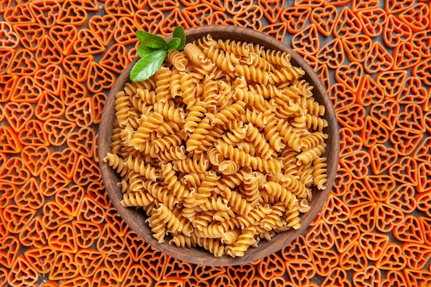 Top view a bowl of spirali pasta on heart shaped italian pasta on dark table