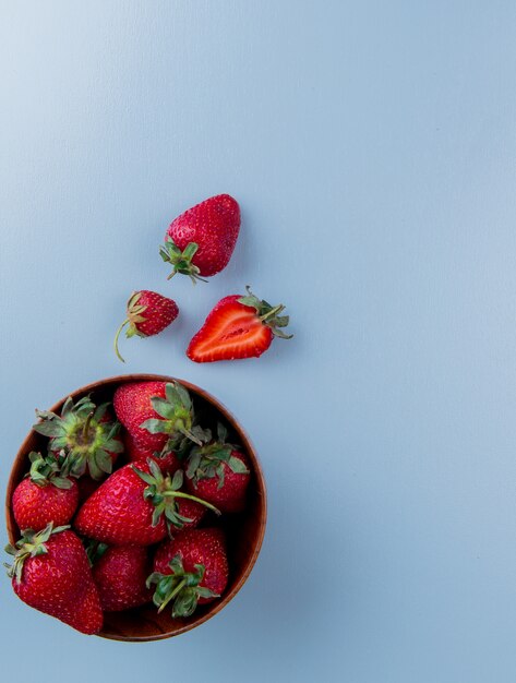 Top view of bowl of strawberries on blue surface with copy space