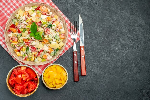 Top view of bowl of vegetable salad on red napkin with veggies and cutleries on side and with free place for text on dark table