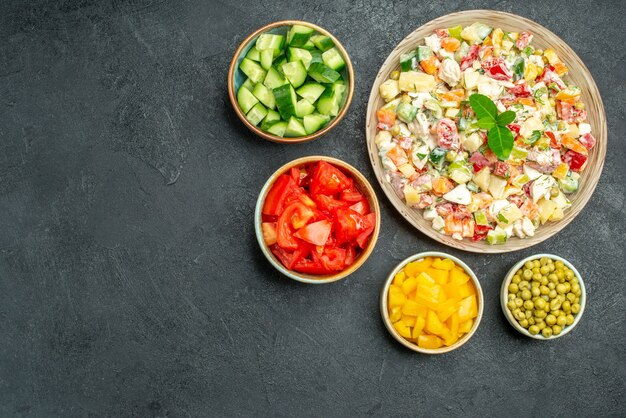 Top view of bowl of vegetable salad with bowls of vegetables on side on dark green background