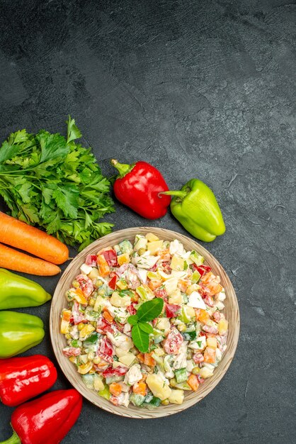 Top view of bowl of vegetable salad with carrots greens and bell peppers on side on dark grey table