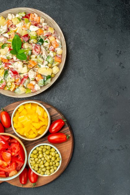 Top view of bowl of vegetable salad with plate stand of vegetables on side and free space for your text on dark grey background