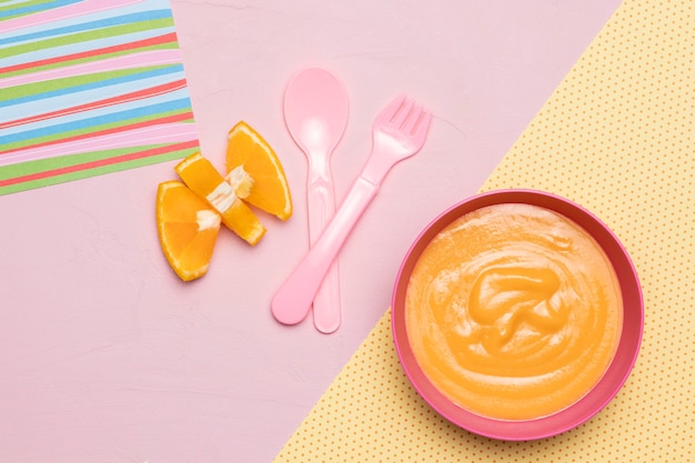 Top view of bowl with baby food and fruit with cutlery