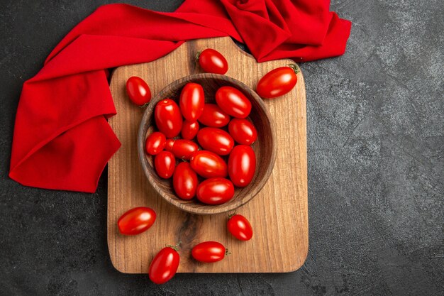 Top view bowl with cherry tomatoes and red towel on a chopping board on dark background