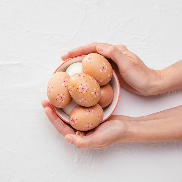 Top view of bowl with decorated easter eggs in hands