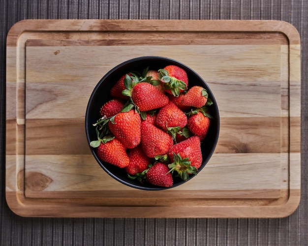 Top view of a bowl with fresh strawberries on a wooden cutting board