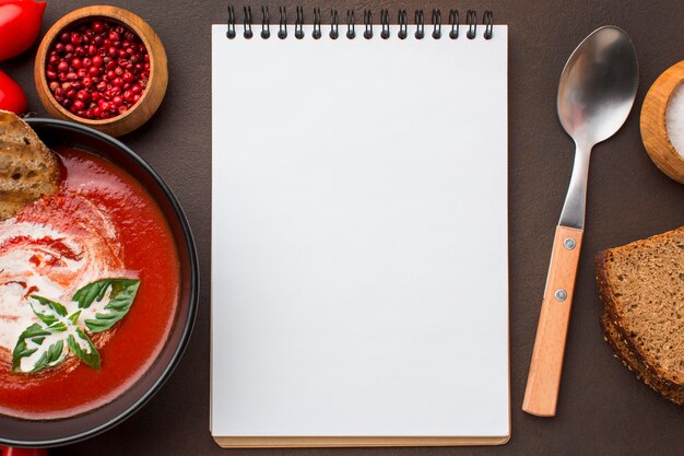 Top view of bowl with winter tomato soup and notebook