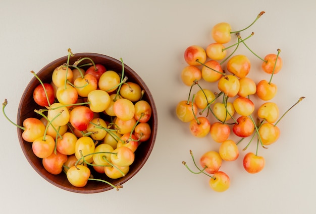 Top view of bowl of yellow cherries with cherries on white surface