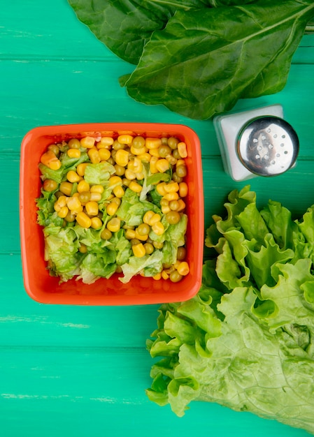 Free photo top view of bowl of yellow pea with sliced lettuce and spinach salt whole lettuce on green