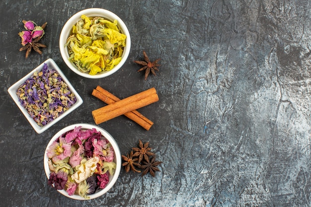 Top view of bowls of dry flower and anise and cinnamon sticks on grey ground