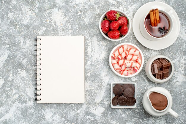 Top view bowls with cacao candies strawberries chocolates tea with cinnamon and a notebook on the grey-white table with free space