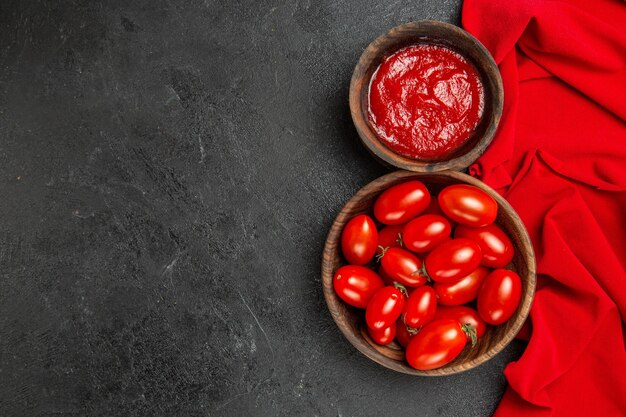 Top view bowls with cherry tomatoes and ketchup and red towel on dark background
