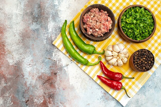Top view bowls with meat greens black pepper hot peppers garlic on kitchen towel on nude background free place