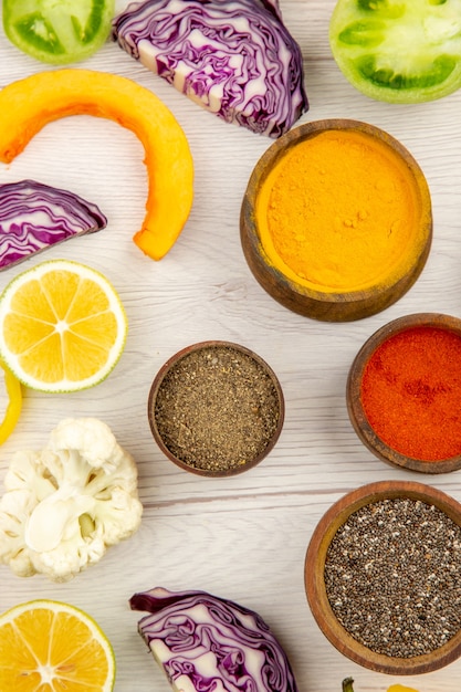 Free photo top view bowls with spices cut bell pepper cauliflower cut red cabbage cut green tomatoes cut lemon on white wooden table