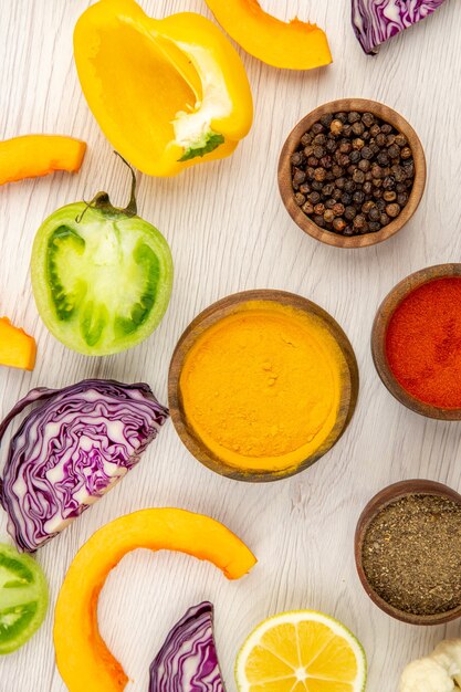 Top view bowls with spices cut bell pepper cut pumpkin cut red cabbage cut green tomatoes cut lemon on white table