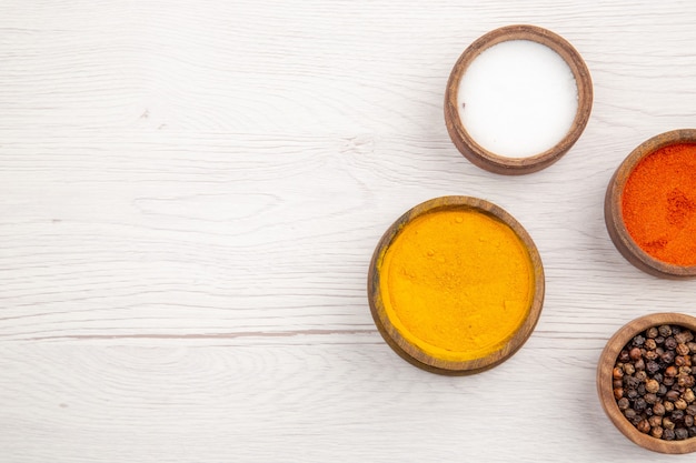 Free photo top view bowls with spices turmeric red pepper powder black pepper salt on grey background