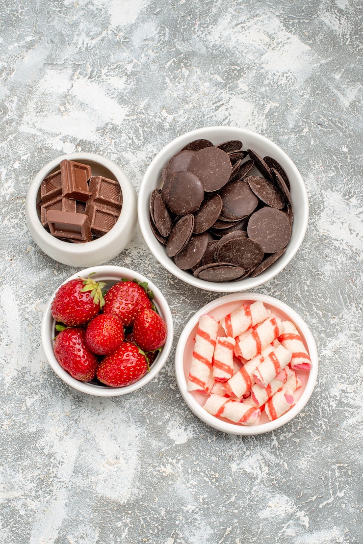 無料Photo 灰色がかった白い地面の中央にイチゴのキャンディーとチョコレートが入った上面図のボウル